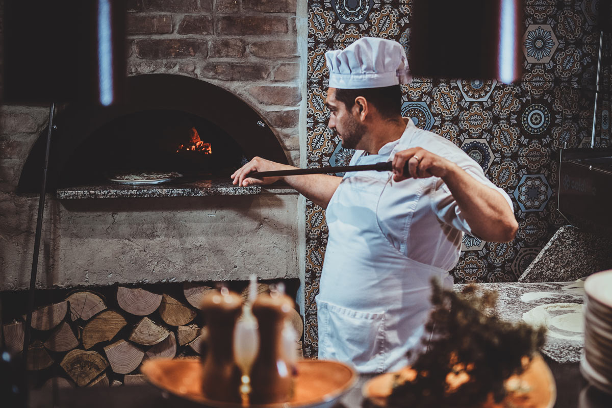 Pizzabäcker-schiebt-Pizza-in-Holzofen